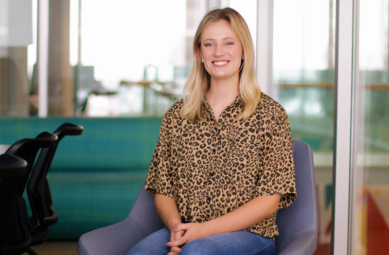 Young woman smiling sitting in a chair wearing a cheetah print blouse.